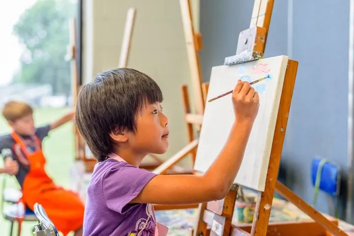 Child painting at an easel during an art class