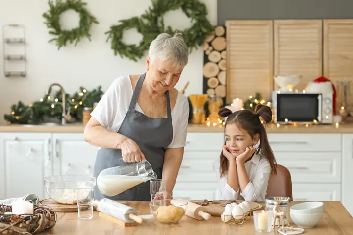 Grandmother and granddaughter baking together in a kitchen decorated with Christmas wreaths