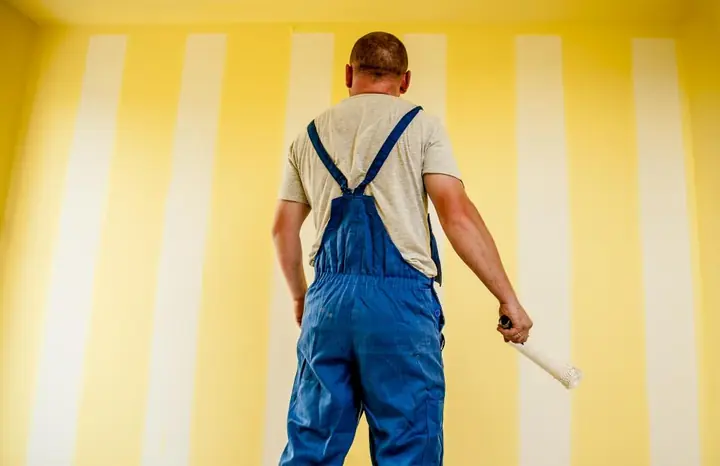 A person rolling cheerful yellow paint onto a living room wall