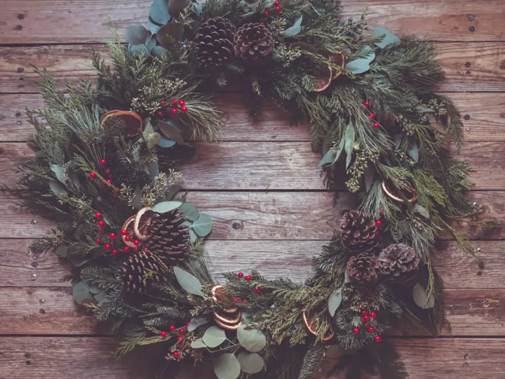 A rustic wreath with greenery and a wooden accent on a wood wall